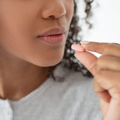 A close-up view captures a moment where a young woman with curly hair is about to consume a small pill, highlighting the importance of health and daily medication adherence, cropped